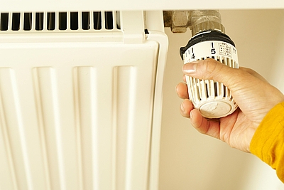 eine Hand dreht an einem Thermostat eines Heizkörpers