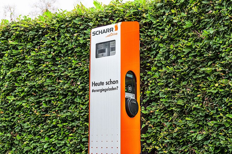 Ladesäule im SCHARR Corporate Design mit orangenen Seiten und dem Spruch "Heute schon energiegeladen?"