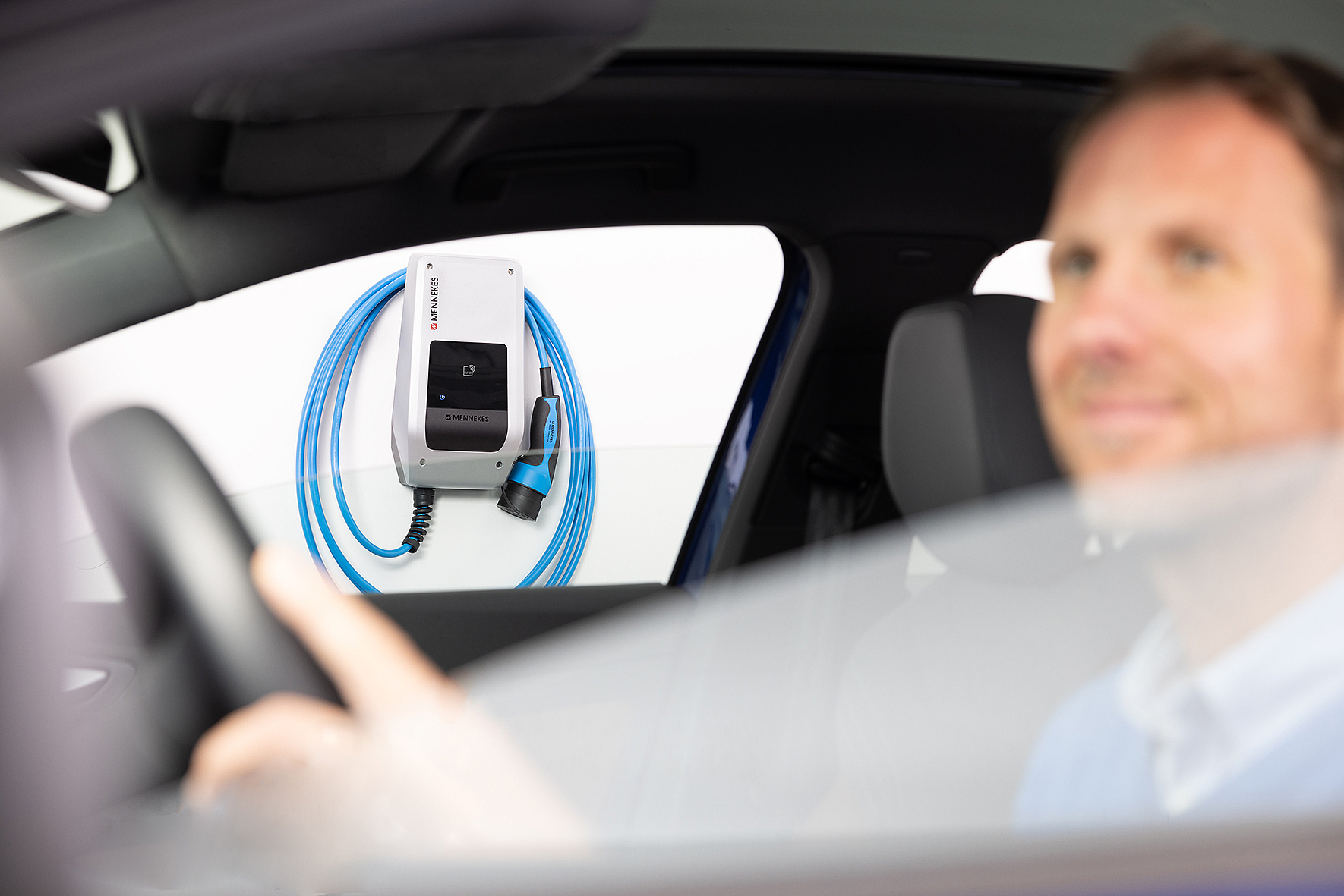Mann im Auto mit Wallbox im Hintergrund